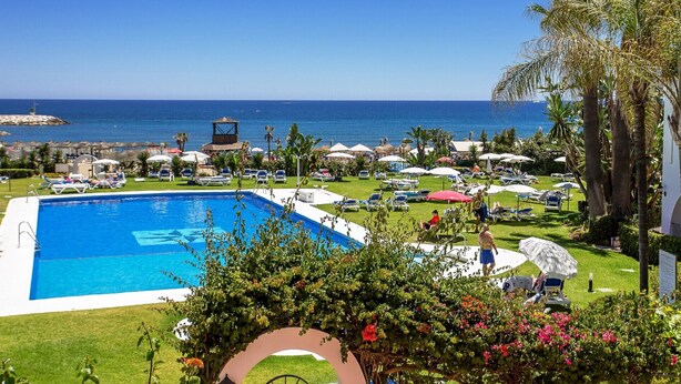 A resort pool with a view of the sea, surrounded by lounge chairs and umbrellas. - D13-2 Cabopino (Marbella)