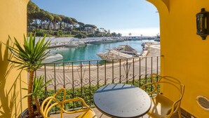 A balcony with a view of a marina, a table, chairs, and a potted plant. - D13-2 Cabopino (Marbella)