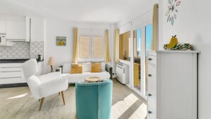 Un soggiorno moderno con un divano bianco, un poggiapiedi color petrolio e un'area pranzo con un armadietto bianco e una ciotola gialla sopra.