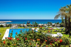Un área de piscina con vista al mar, rodeada de sillas de descanso y sombrillas.