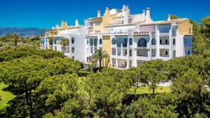 A multi-story building with balconies, surrounded by greenery and a clear sky. - N07 Cabopino (Marbella)