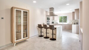 A modern kitchen with a marble countertop, wooden cabinets, and a built-in bar area with stools. - N07 Cabopino (Marbella)