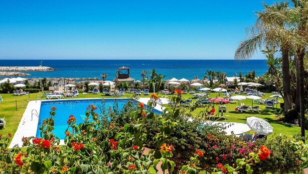 A pool area with a view of the sea, surrounded by lounge chairs and umbrellas. - K105 Cabopino (Marbella)