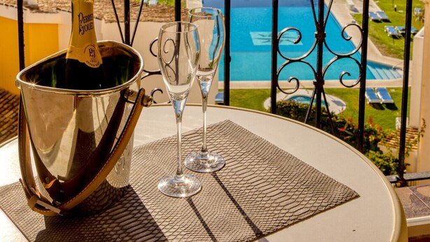 A balcony with a view of the beach and pool, a bottle of champagne, and a glass.