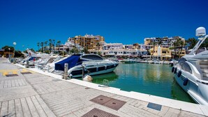 A marina with boats docked, a clear blue sky, and buildings in the background.