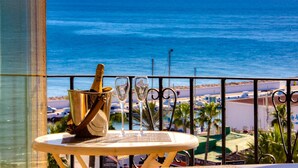 A balcony with a view of the ocean, a table with a champagne bottle and glasses, and a metal railing.