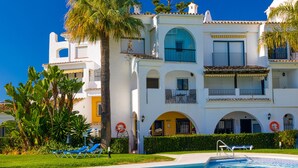 Un hotel a più piani con balconi, piscina e palme.