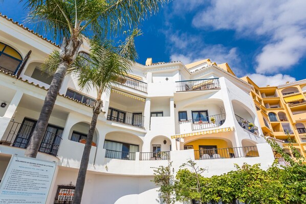 A multi-story hotel with balconies, a pool, and a sign indicating rules for the pool area. - L168 Cabopino (Marbella)