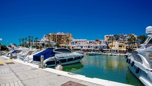 A marina with boats docked, a clear blue sky, and buildings in the background. - L168 Cabopino (Marbella)