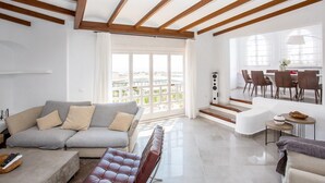 A spacious living area with a grey sofa, a red leather ottoman, and a dining area with a table and chairs. - L168 Cabopino (Marbella)
