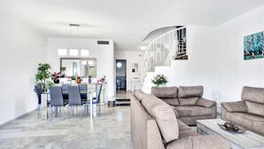 Ett rymligt vardagsrum med en stor beige soffa, en matplats med bord och stolar samt en trappa som leder upp till ett övre plan.