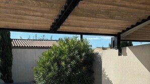 Un patio con una mesa y sillas blancas, una planta en maceta y piso de baldosas.