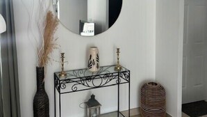 Un interior minimalista con un espejo redondo, una consola decorativa, un jarrón alto y una cesta de mimbre.