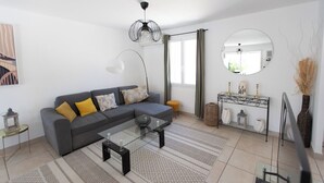 Una sala moderna con un sofá gris, una mesa de centro de vidrio, un espejo redondo y una consola decorativa.
