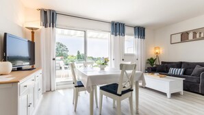 Ett modernt vardagsrum med en matplats, en platt-TV och en balkong med gardiner.