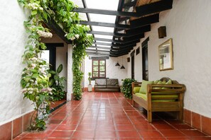 Un couloir avec un sol carrelé, un banc en bois, un canapé et une plante en pot.