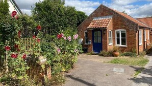 A brick house with a blue door and windows, surrounded by a garden with red flowers.