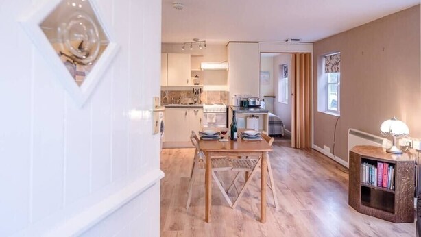 A modern kitchen with a dining area, wooden flooring, and a bookshelf.