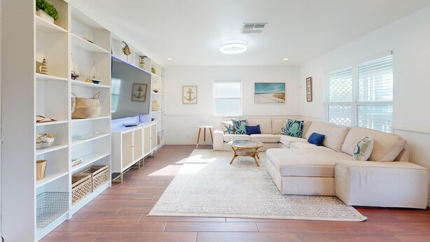 A spacious living room with a beige sofa, a coffee table, and a white bookshelf filled with decorative items. - In Town, Ample Parking, Swing set for Kids, Pet Friendly (Port Aransas)