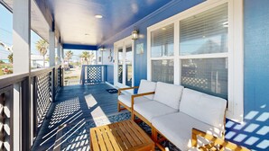 A covered porch with a white sofa and wooden table, blue walls, and large windows. - In Town, Ample Parking, Swing set for Kids, Pet Friendly (Port Aransas)