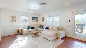 A spacious living room with a sectional sofa, a coffee table, and a large window providing natural light. - In Town, Ample Parking, Swing set for Kids, Pet Friendly (Port Aransas)