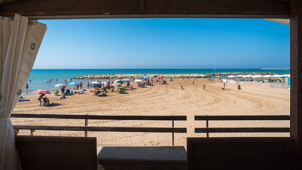 Blick auf einen Strand von einer überdachten Fläche mit Holzgeländer.