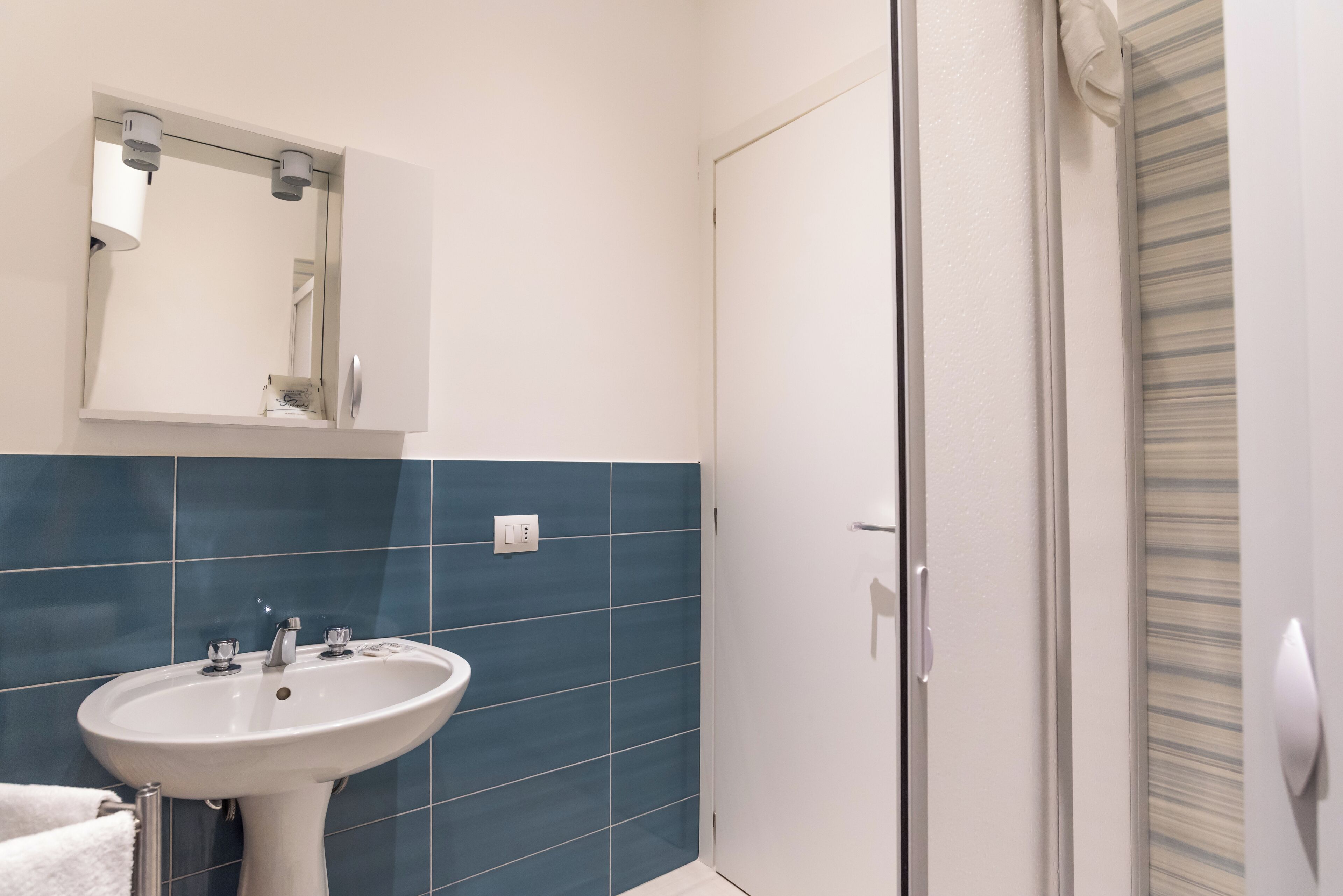Een badkamer met een wit wastafelmeubel, blauwe tegels, een spiegel en een deur.