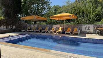 Una piscina al aire libre, sombrillas, sillones reclinables de piscina