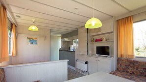 A compact kitchen with a built-in stove, a microwave, and a small refrigerator. There is a dining table with a bench, and a TV mounted on the wall. - Island of Rügen by the lake, only 10 minutes from the Baltic seaside resort of Binz (Zirkow)