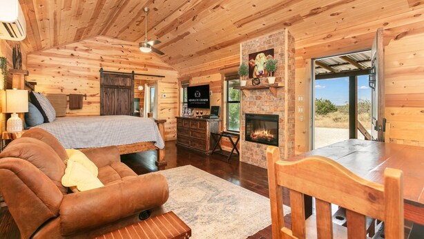 Interior de una cabaña de troncos con cama, sofá, chimenea y comedor.