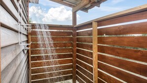 Un área de ducha exterior de madera con un estante metálico y un caño.