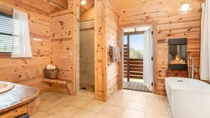 Baño de cabaña de madera con ducha, chimenea y bañera.