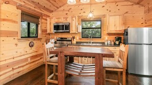 Interior de una cabaña de madera con cocina, que incluye una mesa de comedor, sillas, un refrigerador y un microondas.