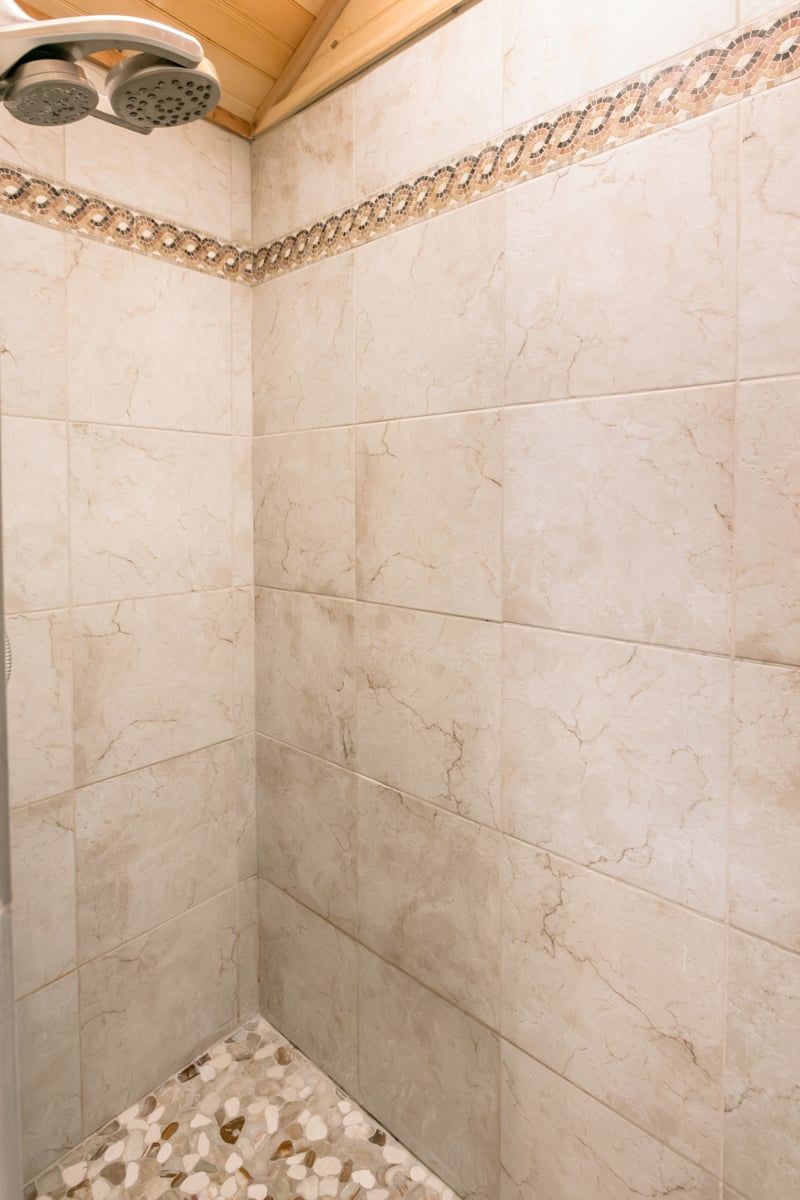 A shower area with beige tiles and a mosaic border.