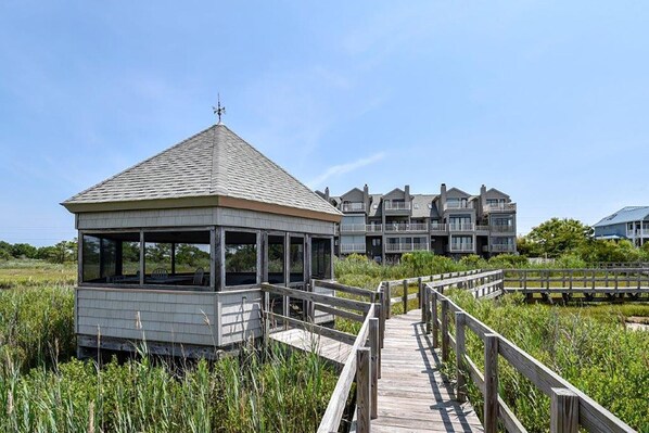 A wooden gazebo with a metal roof and a wooden walkway leading to a beachfront property.