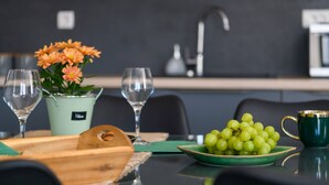 Een eettafel met een groene schaal groene druiven, een groene mok en twee wijnglazen.
