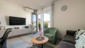 Een moderne woonkamer met een flatscreen televisie, een groene fauteuil, een bruine bank en een klein rond tafeltje met een vaas.