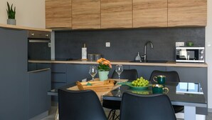 Een moderne keuken met donkere kastjes, een houten aanrecht, een ingebouwde oven, een magnetron, en een eethoek met een tafel gedekt voor twee personen.