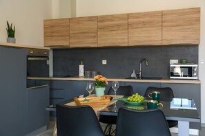 A modern kitchen with dark cabinets, a wooden countertop, a built-in oven, a microwave, and a dining area with a table set for two. - NEW Villa Dora - Apartment 1 "Green" with terrace and barbecue (Pula)