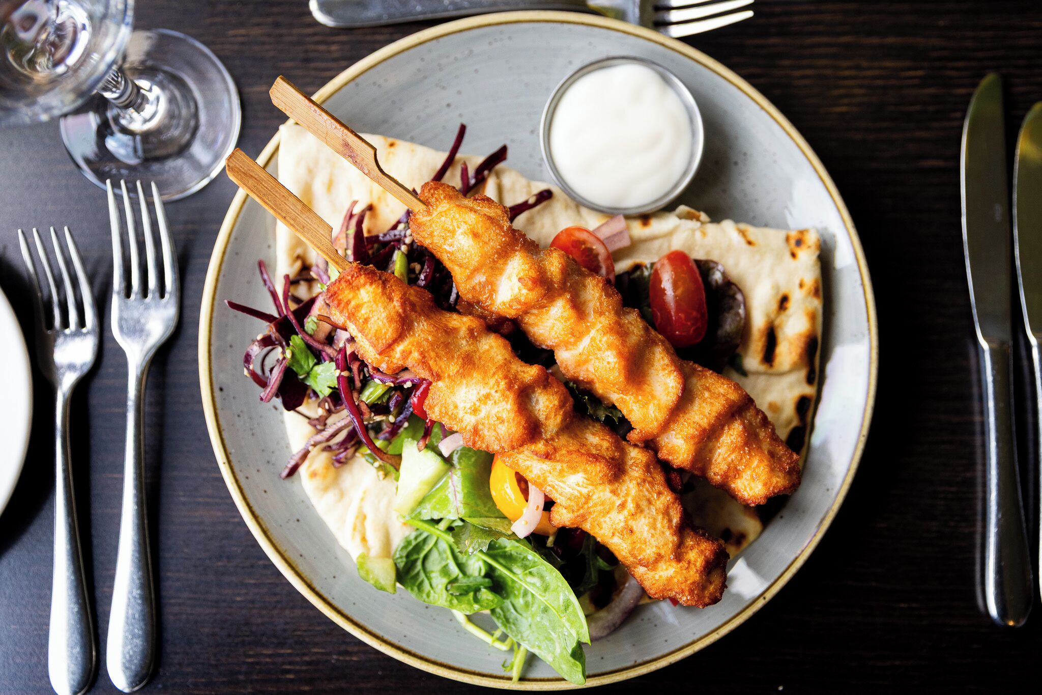A plate with food, a fork, a knife, and a glass of water on a table.
