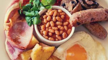 A plate of breakfast food including eggs, bacon, sausages, mushrooms, tomatoes, beans, and greens.