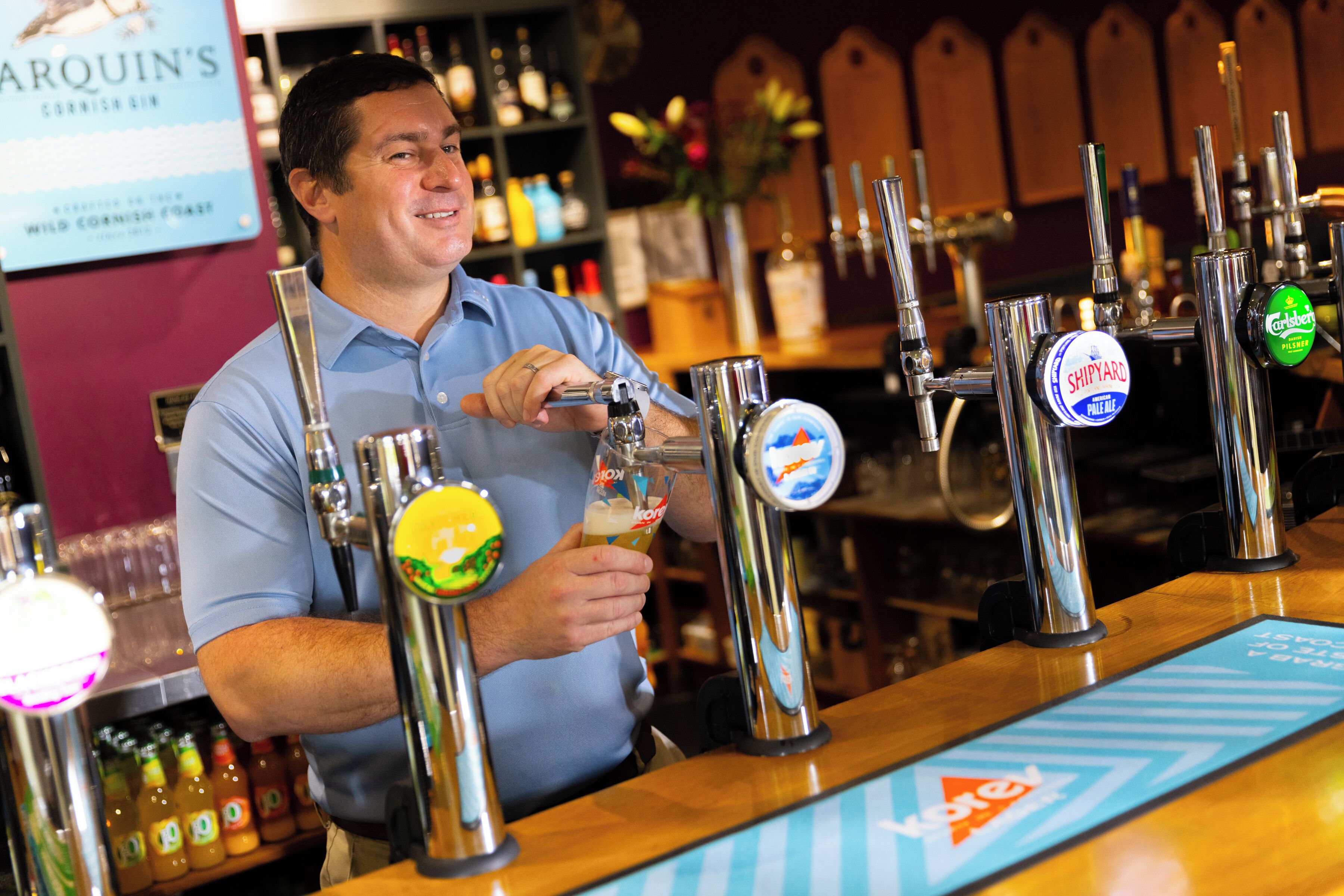 A bartender at a bar with multiple beer taps and a variety of bottles in the background.