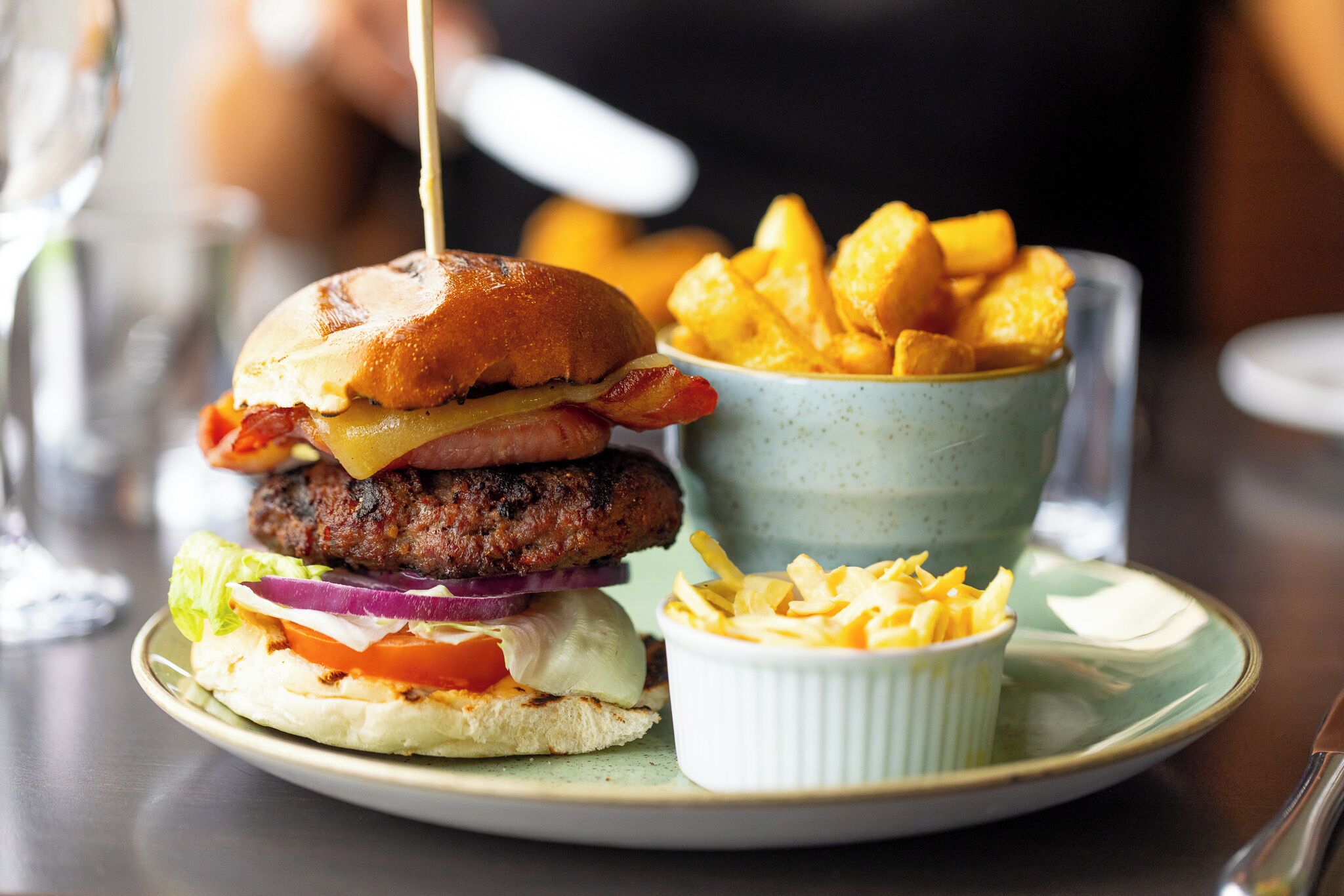 A plate with a burger, fries, and a small bowl of sauce.