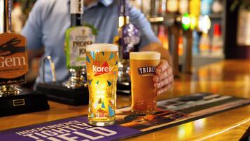 Un bar con dos vasos de cerveza, una llave de cerveza con la etiqueta 'Gem' y un posavasos con el texto 'Independence Tight Held'.
