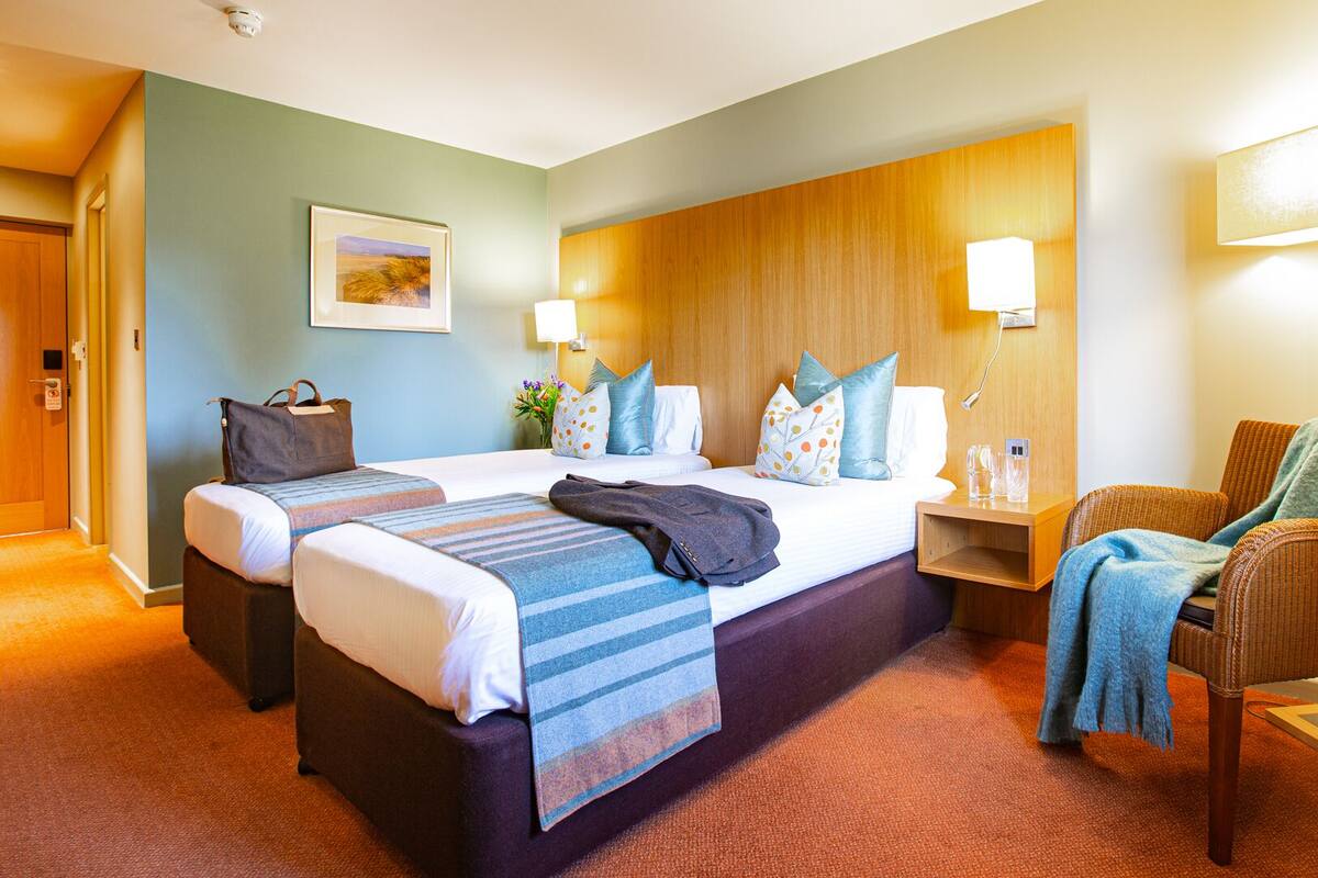 A hotel room with a large bed, two bedside tables, a chair, and a wall-mounted lamp.