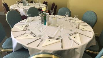 A round dining table set with white tablecloth, silverware, and wine glasses, surrounded by blue upholstered chairs.