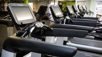 A row of treadmills in a gym with a green wall and a television screen.