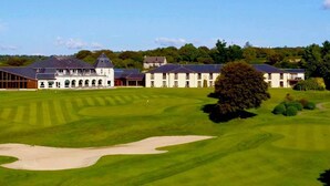 A golf course with a clubhouse featuring multiple buildings and a large tree in the foreground. - Lanhydrock Hotel and Golf Club (Bodmin)