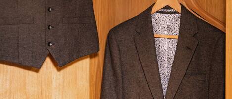 A wooden wardrobe with two hangers, one holding a dark brown suit jacket and the other a brown leather bag.