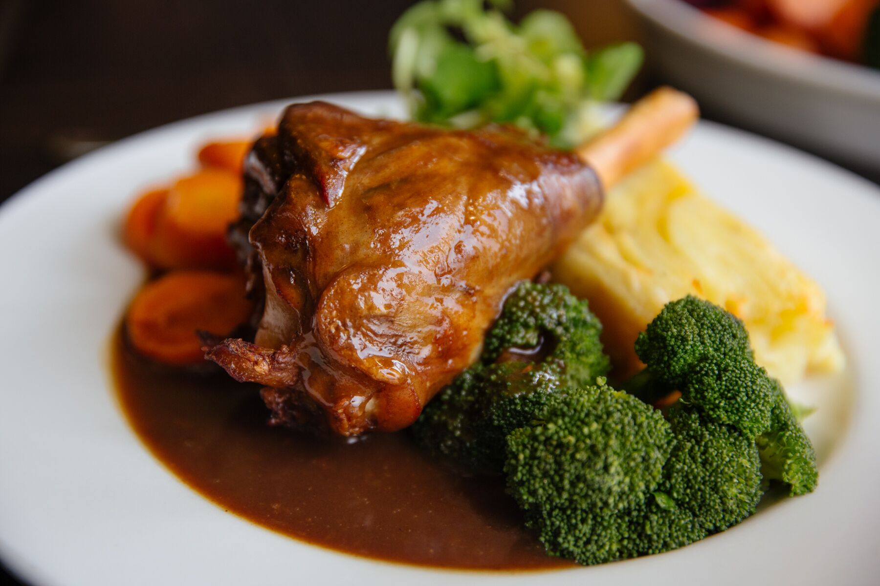 Une assiette contenant un gigot d’agneau rôti, des carottes, des brocolis et de la purée de pommes de terre.